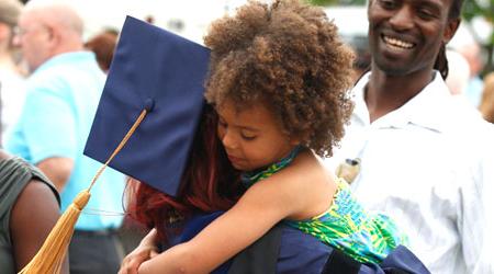 Xavier graduate in their cap and gown hugging a small child
