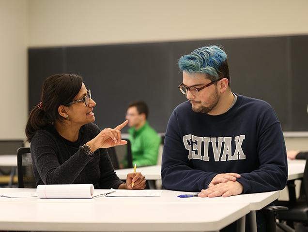 A Xavier student working with a professor at a desk in a classroom