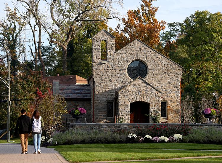 Two students walk toward Dana Avenue, passing Our Lady of Peace Chapel