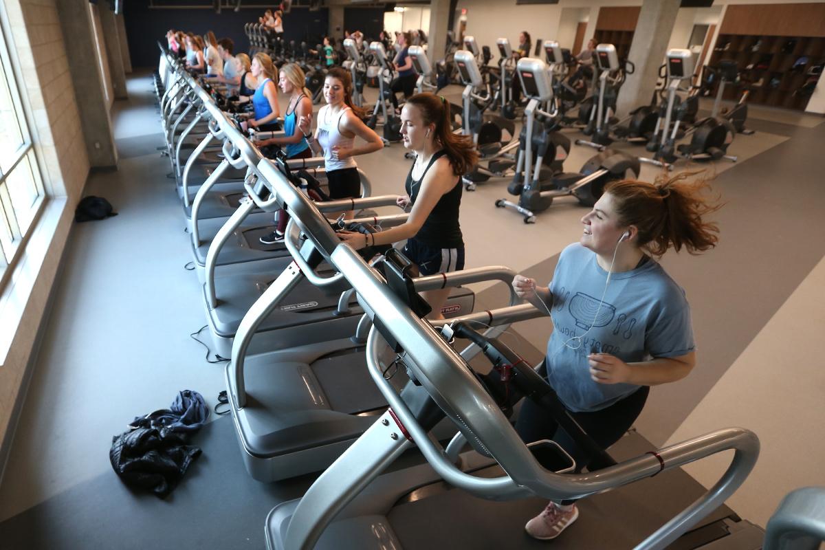 学生们在健康联合大楼的一排跑步机上跑步. 后面是一排排的锻炼背.