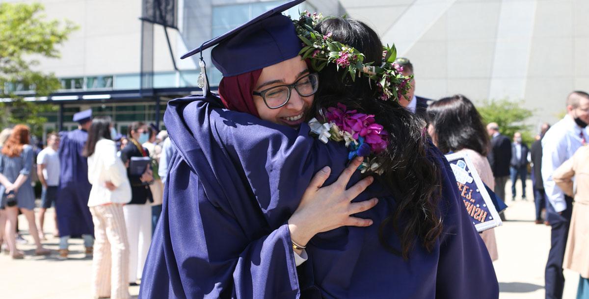 Two Xavier graduates hug on their graduation day. They are both wearing navy blue graduation caps and gowns.