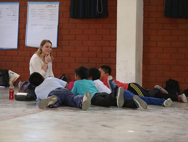 A teacher leading a lesson plan. A group of children are sitting in front of the teacher.