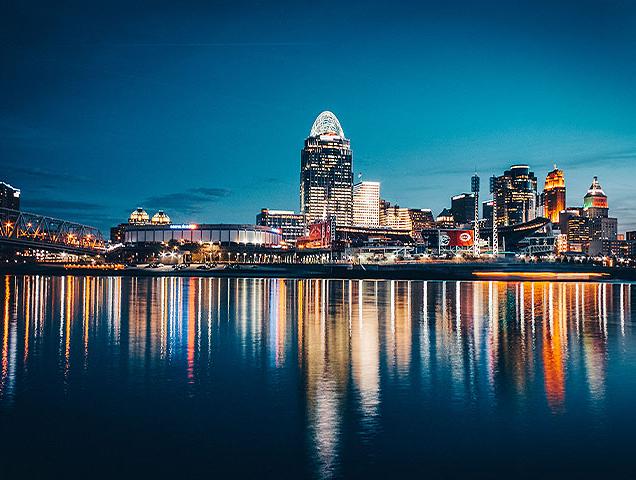 Downtown, Cincinnati skyline at nighttime. Lights reflect on the Ohio River.